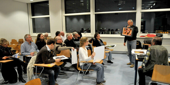 Mitglieder des Fotoklubs in sitzen in einem Seminarraum und diskutieren Fotos aus einer Fotomappe
