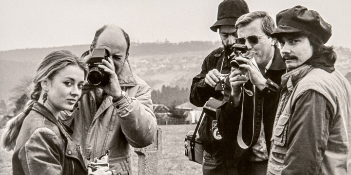 schwarz-weiß Aufnahme im Freien, vier Männer und eine Frau mit Fotoapparaten, die Frau wird von zwei der Männer fotografiert. 