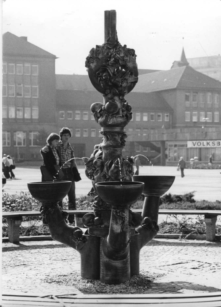 figürlich gestalteter Marktbrunnen auf dem Platz der Kosmonauten in Jena und vorbeilaufende Menschen im Hintergrund